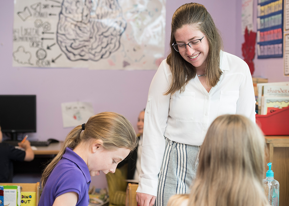 Student teacher smiles at two students in a classroom